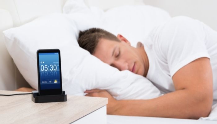 a smartphone is being charged beside a person sleeping